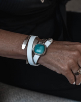 Close-up of a wrist wearing a white leather bracelet with a turquoise stone and a silver ring.