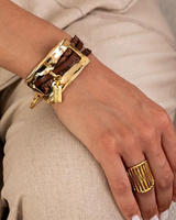 Hand wearing a gold bracelet and ring on a neutral background