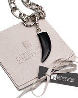 Chunky steel chain necklace featuring a black agate tooth pendant with U-bolt shackle detail, presented in a suede pouch.