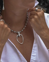 Layered silver ball chain choker with a hammered loop pendant; worn with a white collared shirt.