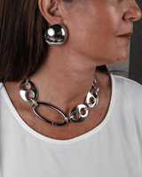 Oversized dome stud earrings in polished metallic finish, worn with a modern chain necklace against a white top.