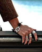 Hand with multiple bracelets and rings on a metallic surface with a blurred background