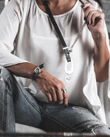 Person wearing a white shirt and jeans, holding a necklace with a pendant.