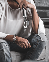 Person wearing a white shirt and ripped jeans with accessories, sitting on a checkered chair.