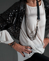 Person wearing a black sequin jacket over a white top with layered necklaces on a gray background