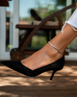 Silver snake chain anklet worn on the ankle, paired with a black pointed-toe heel, showcasing an elegant and edgy look.