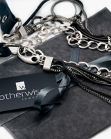 Silver chain necklaces on a gray surface with 'otherwise' jewelry card.