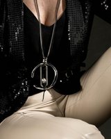 Person wearing a black sequin top and beige pants with a prominent necklace.