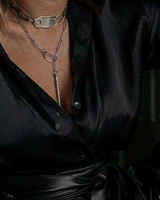 Person wearing a black satin outfit with jewelry and tattoos.