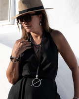 Woman wearing a black sleeveless top, beige hat, and sunglasses against a white wall.