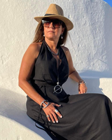 Woman in a black dress and hat sitting on a white wall with a blue sky background