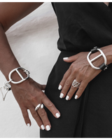 Close-up of hands wearing silver bracelets and rings on a neutral background