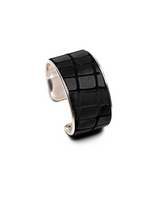 A wide silver cuff ring featuring a textured black exterior with a raised grid pattern, shown on a plain white background.