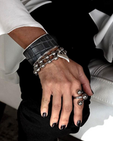 Hand wearing multiple bracelets and rings with a blurred background