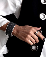 Person wearing a white shirt with a black jacket featuring large buttons, holding a metallic object.