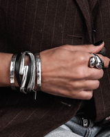 Black leather wrap bracelet featuring a natural leather strand and snake chain, layered with silver metal cuff bracelets.