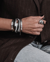 Black leather wrap bracelet featuring a strand of leather and snake chain, worn stacked with silver bangles on a wrist.