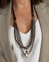 Necklace with multiple chains and pendants worn by a person in a beige blazer and white shirt.
