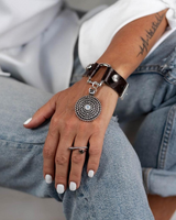 Brown leather horsebit cuff bracelet featuring a silver spiral pendant with a white opal crystal, worn on a model's wrist.