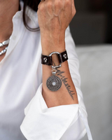 Brown leather cuff bracelet featuring a horse bit buckle and white opal pendant, worn with a white shirt.