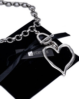 Chunky heart statement set featuring a silver-tone choker with a hammered heart pendant, displayed on a black suede pouch.