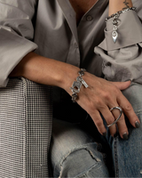 Person wearing a gray shirt and jeans with jewelry sitting on a patterned couch.