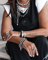 Person wearing multiple necklaces, bracelets, and rings sitting on a couch.