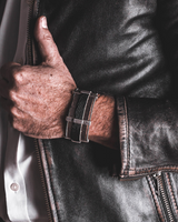 Person wearing a dark leather jacket with a close-up of the sleeve and hand.