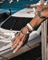 Person's hand with jewelry by a marina with boats in the background