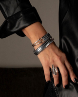 Silver hematite wrap bracelet with polished beads, worn layered with metal cuffs, showcased on a hand with dark nail polish.