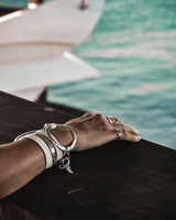 Hand with multiple bracelets on a railing by water