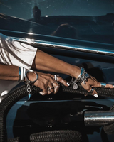 Person's hand with multiple bracelets and rings on a car door handle