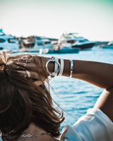 Person with silver bracelet and ring by a marina with yachts