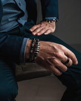 Silver leather men’s bracelet on a model's wrist, paired with two other bracelets and a dark suit.