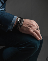 Silver leather men’s bracelet features dark brown PU leather with strong silver-plated metal elements, worn with layered bracelets.