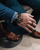 Silver leather men's bracelet featuring dark brown PU leather and silver-plated metal, worn with layered black beaded bracelets.