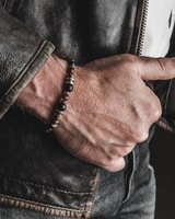 Hand wearing a beaded bracelet with a leather jacket background