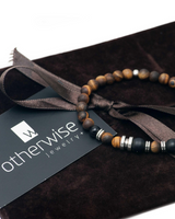 Beaded bracelet with 'otherwise jewelry' card on a brown fabric background