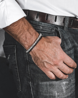 Person wearing a white shirt and dark jeans with a belt, sitting on a couch.