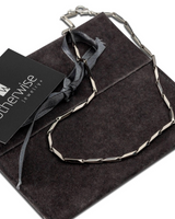 Silver necklace on a dark fabric with 'otherwise jewelry' card