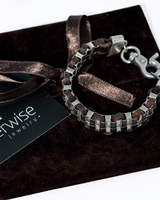 Bracelet with brown leather strap and silver chain on a dark surface with 'otherwise jewelry' card.