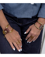 Close-up of hands wearing gold bracelets and rings on a neutral background