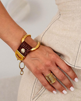Hand wearing a gold bracelet and ring on a neutral background
