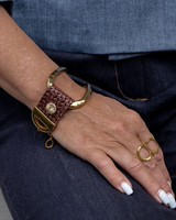 Hand wearing a brown woven bracelet and gold ring on a dark background