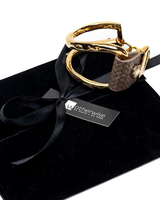 A gold-tone metal horse bit with a textured and woven brown leather cheekpiece, presented on a black velvet gift pouch with a black ribbon and a Wetherwise Equine tag.
