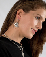 Contemporary statement earrings featuring a coin pendant, displayed on a model with a sleek hairstyle.