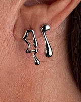 Silver earrings shaped like teardrops worn on an ear