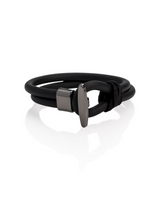A black wrap bracelet with a matte dark gray metal clasp, displayed on a clean white background with a soft reflection.