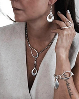 Woman wearing silver jewelry including earrings, necklace, and bracelet on a neutral background