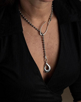 Person wearing a black top with a deep neckline, showcasing a silver necklace with a teardrop pendant.